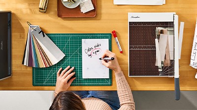 Clean desk with a woman writing on a Quartet notepad